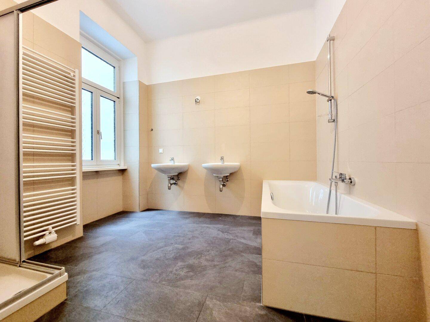 Geräumiges Badezimmer mit Badewanne, zwei Waschbecken und beigefarbenen Fliesen.