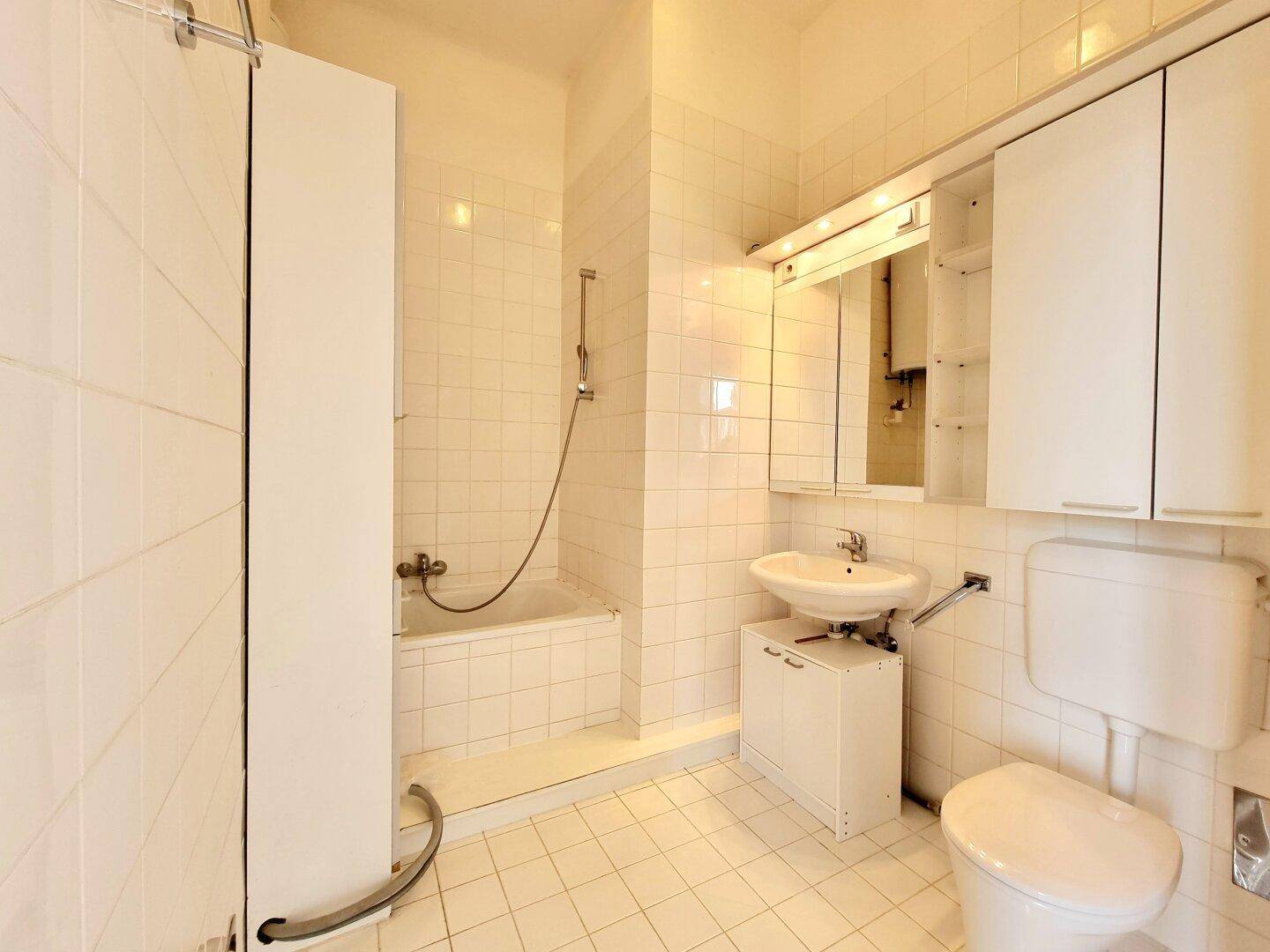 Funktionales Badezimmer mit weißen Fliesen, Badewanne mit Duschfunktion und praktischem Spiegelschrank.