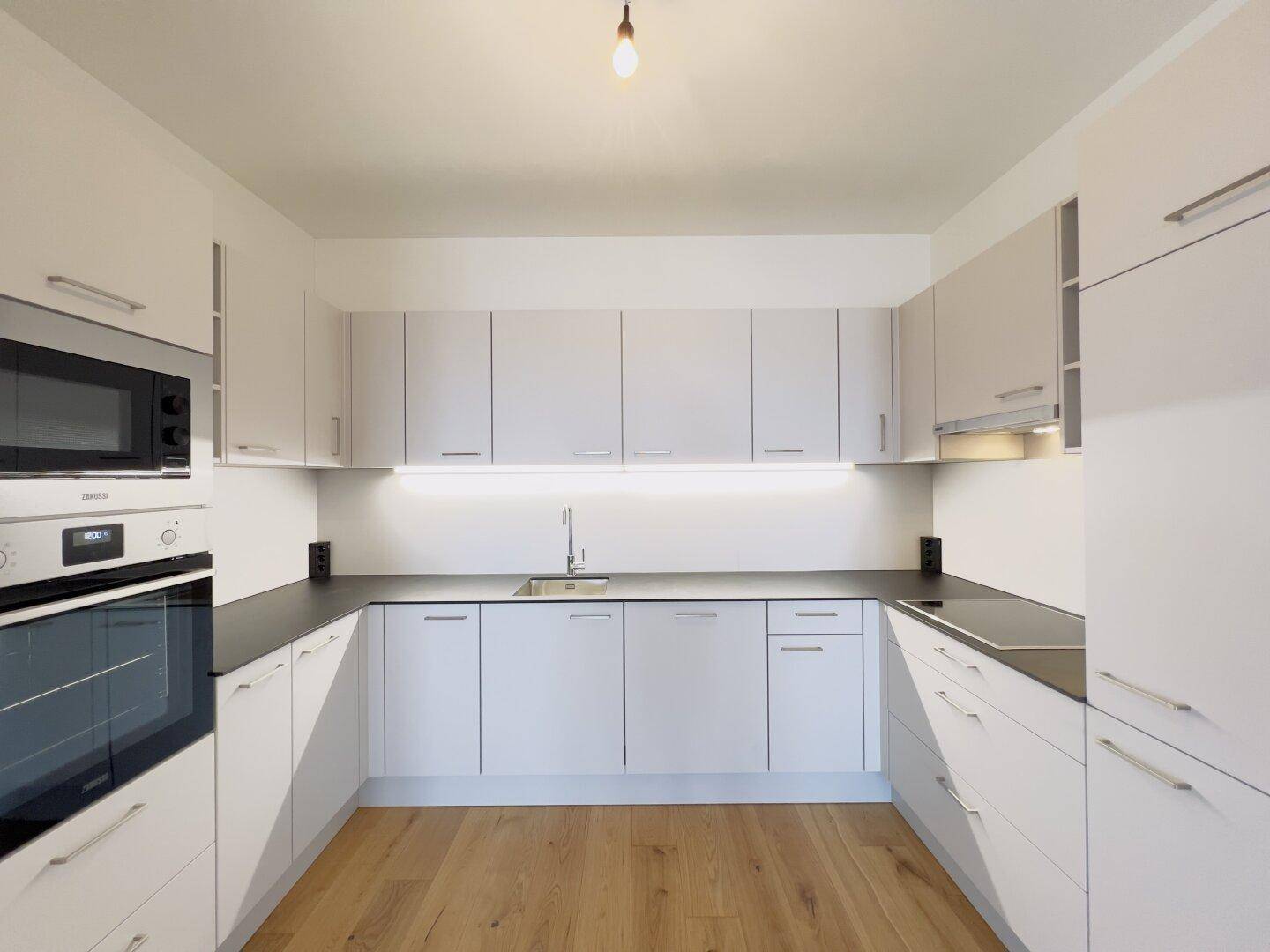 Moderne Einbauküche mit weißen Schränken, dunkler Arbeitsplatte und integrierten Geräten.
