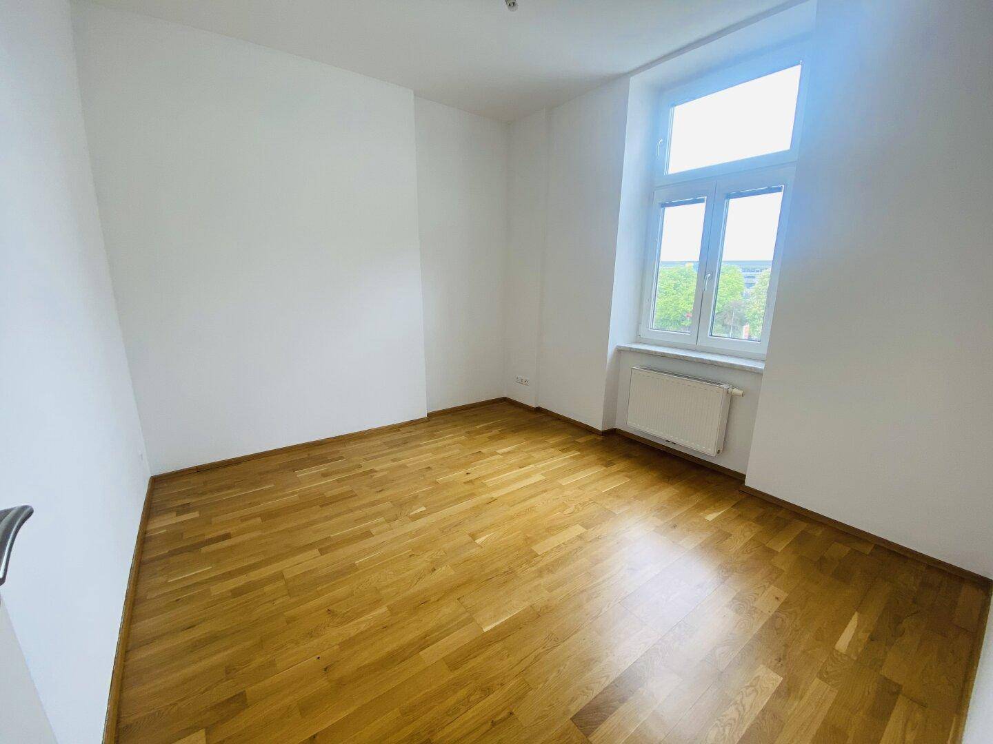 Geräumiges Zimmer mit hellem Parkettboden, weißen Wänden und einem großen Fenster für viel Tageslicht.