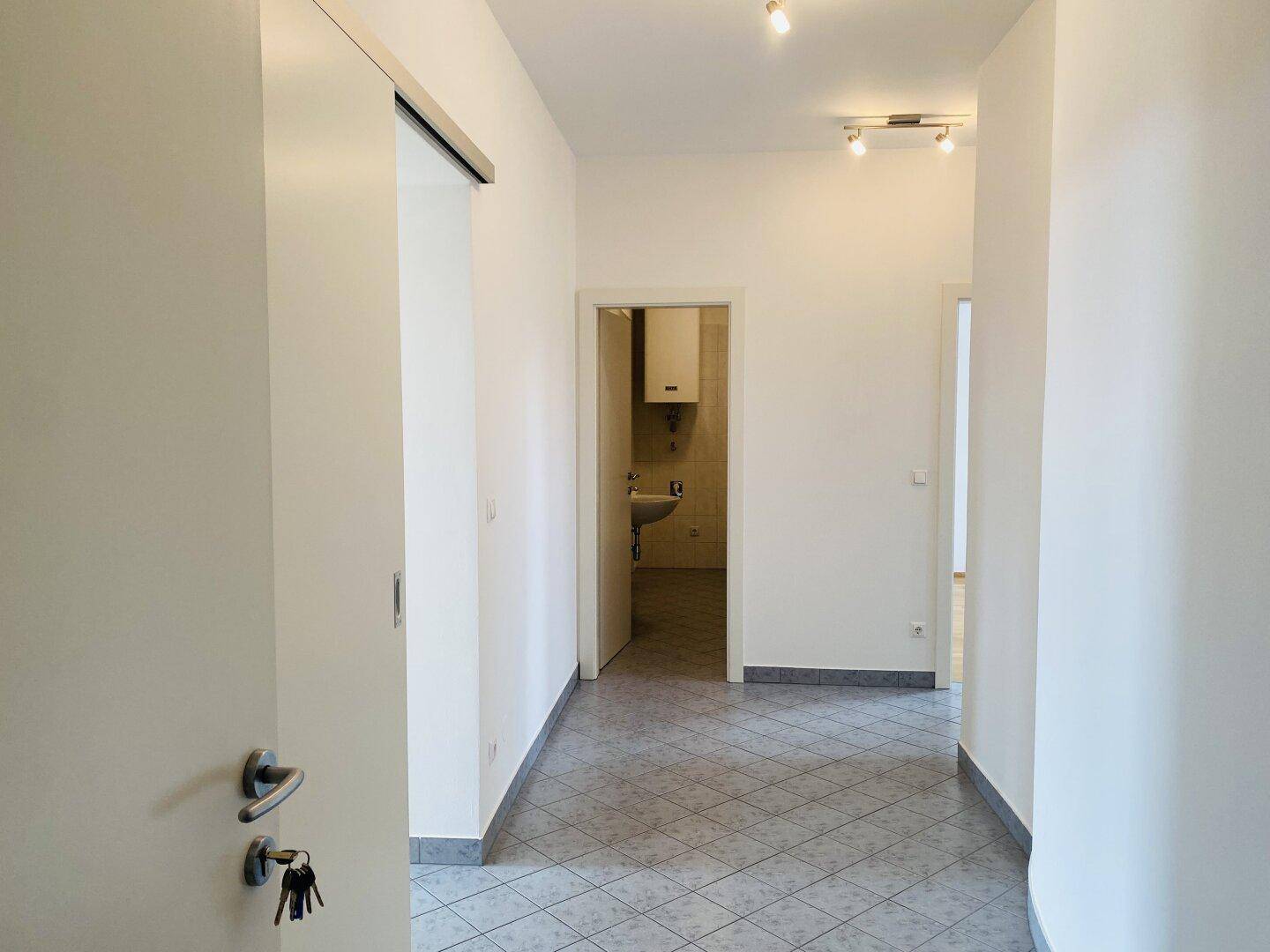Heller Flur mit Fliesenboden und Zugang zu weiteren Räumen, inklusive Blick auf ein Badezimmer.
