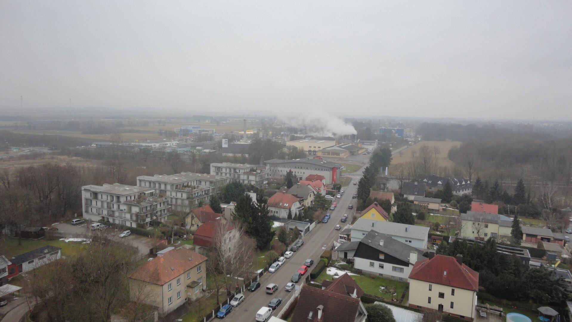 Weitläufige Luftaufnahme einer Vorstadtlandschaft mit Wohngebäuden und Industrie im Hintergrund.