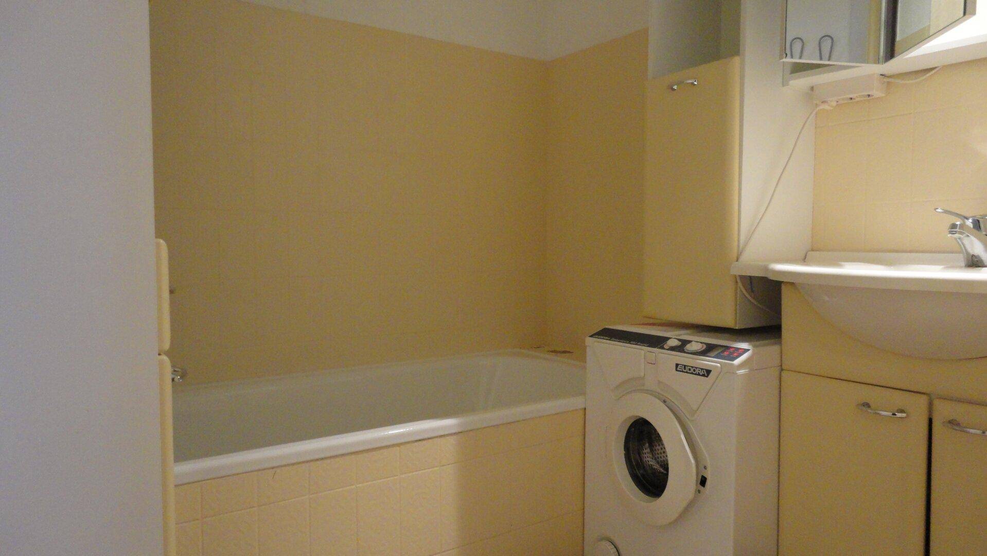 Badezimmer mit Badewanne, Waschbecken, Spiegelschrank und Waschmaschine in warmen Gelbtönen.