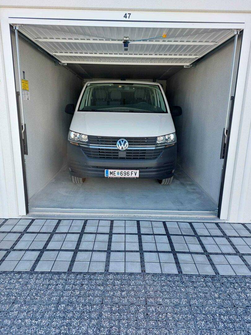 Ein weißer Volkswagen Transporter steht in einer sauberen, hellen Garagenbox mit offenem Rolltor und Betonboden.