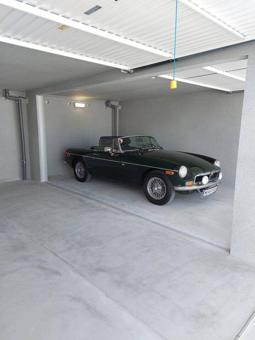 Geräumige Garage mit einem klassischen grünen Sportwagen und sauberem Betonboden.