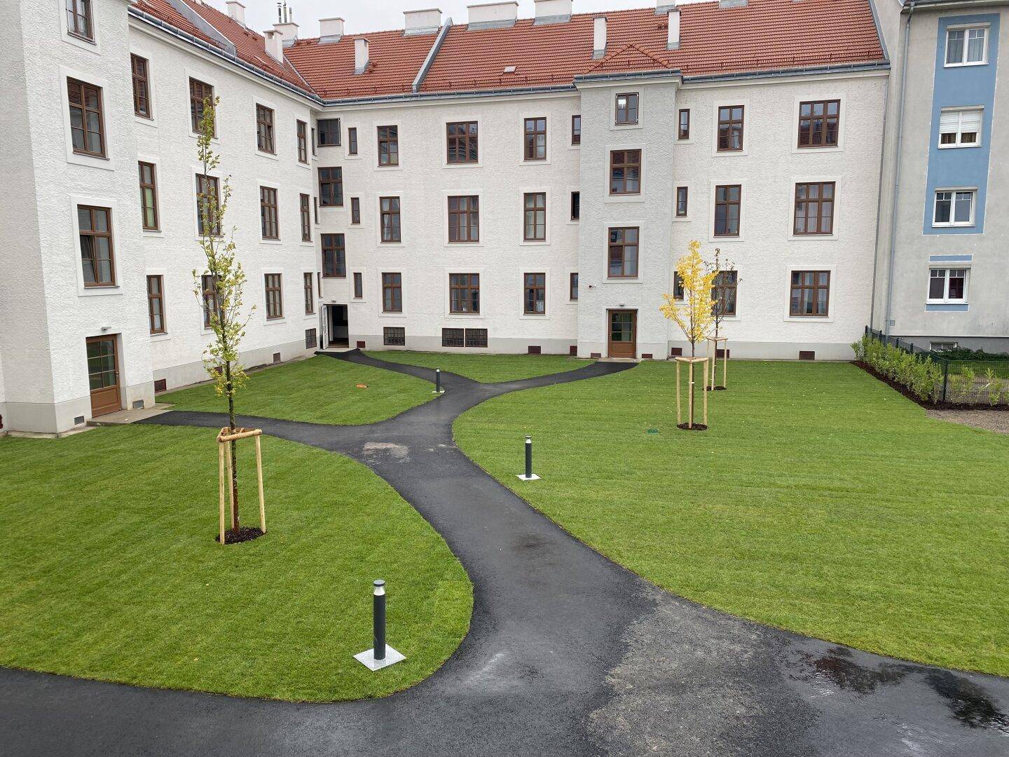 Gepflegter Innenhof mit Rasenflächen und jungen Bäumen, umgeben von Wohngebäuden.