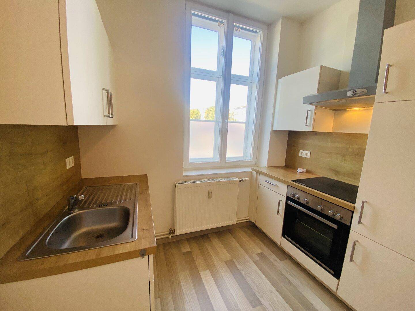 Funktionale Küche mit hellen Schränken, Holzoptik-Arbeitsplatte und integriertem Backofen.