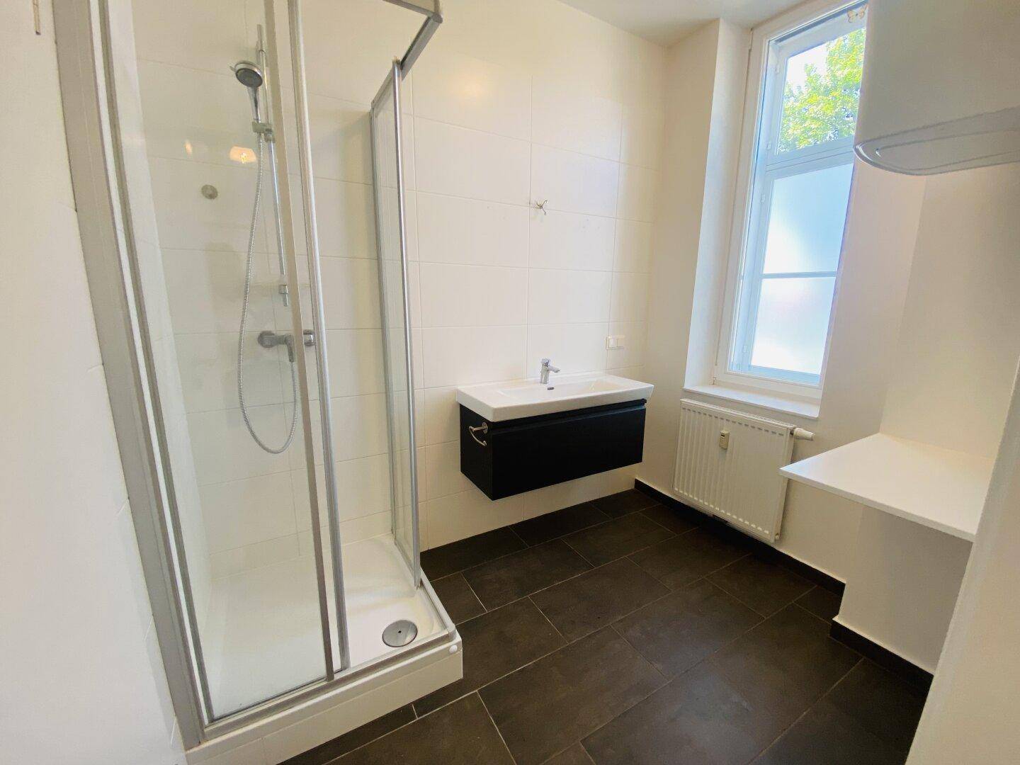 Modernes Badezimmer mit Dusche, dunklen Fliesen und Fenster für Tageslicht.