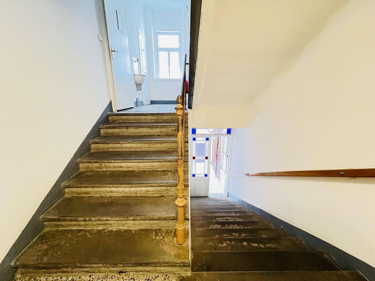 Treppenhaus mit Steinstufen und Holzgeländer, das zu den oberen Etagen führt und natürliches Licht erhält.