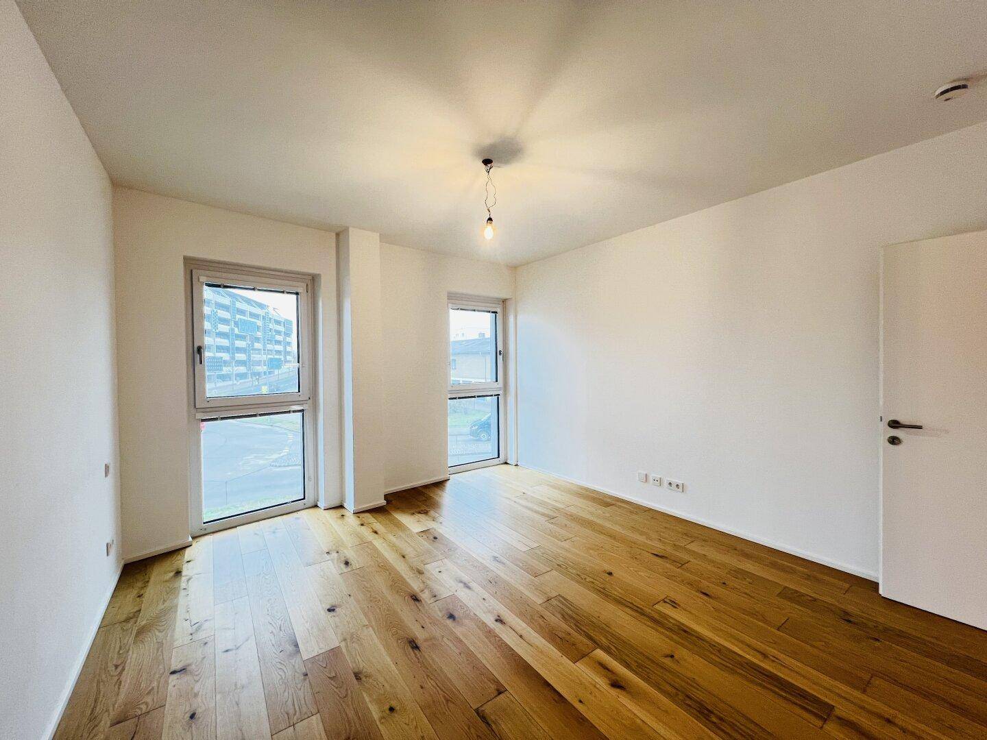 Lichtdurchflutetes Schlafzimmer mit Parkettboden und zwei großen Fenstern.
