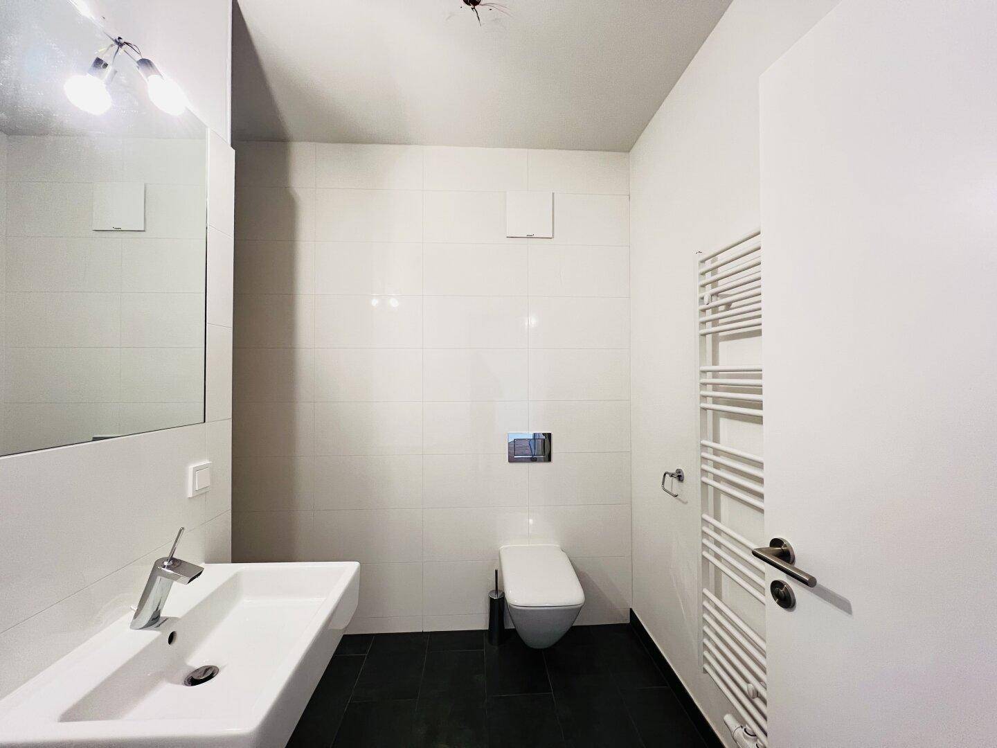 Helles Badezimmer mit wandhängendem WC, modernem Waschbecken und Handtuchheizkörper.