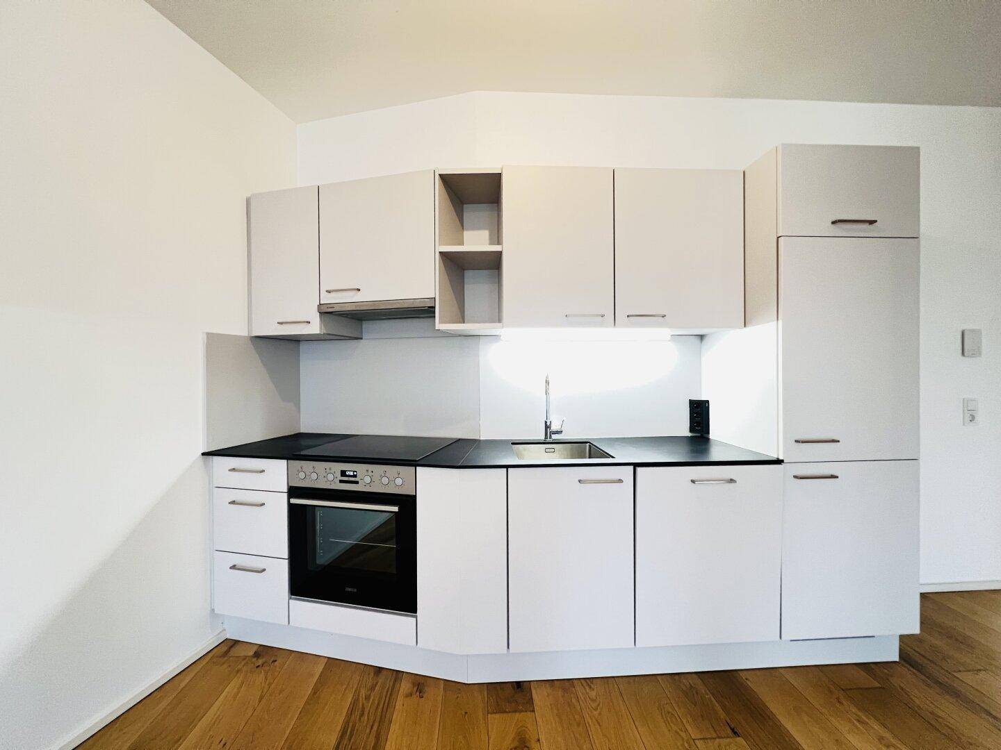Kompakte, moderne Einbauküche mit weißen Schränken, Kochfeld und integriertem Backofen.