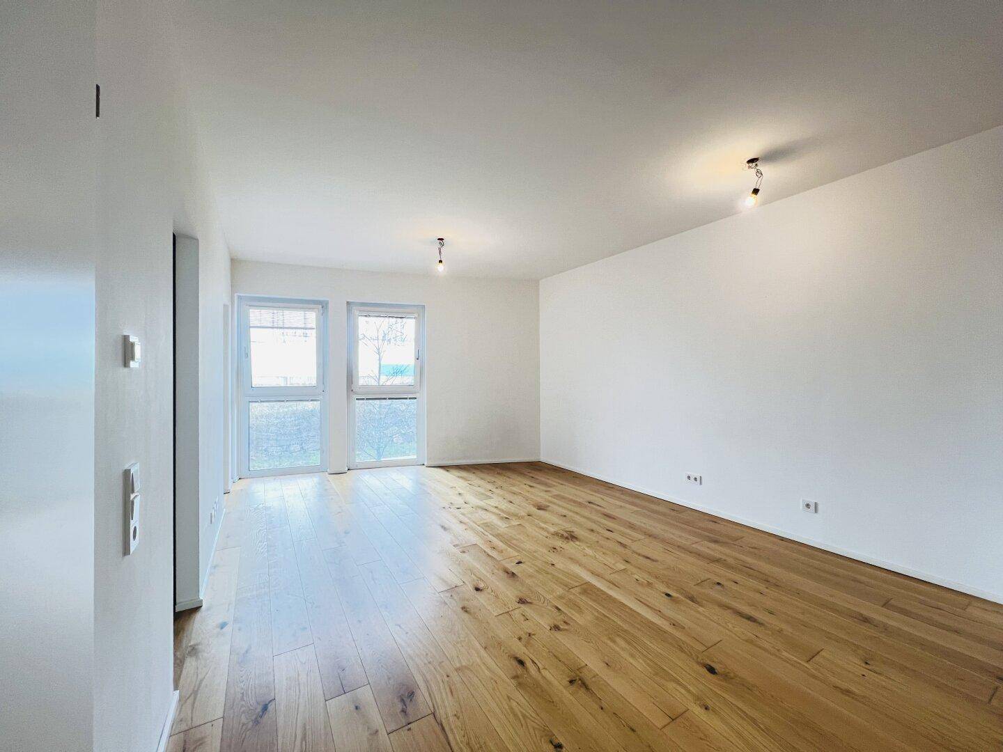 Lichtdurchfluteter Raum mit Holzboden und zwei Glastüren, die Zugang zu einem Außenbereich bieten.