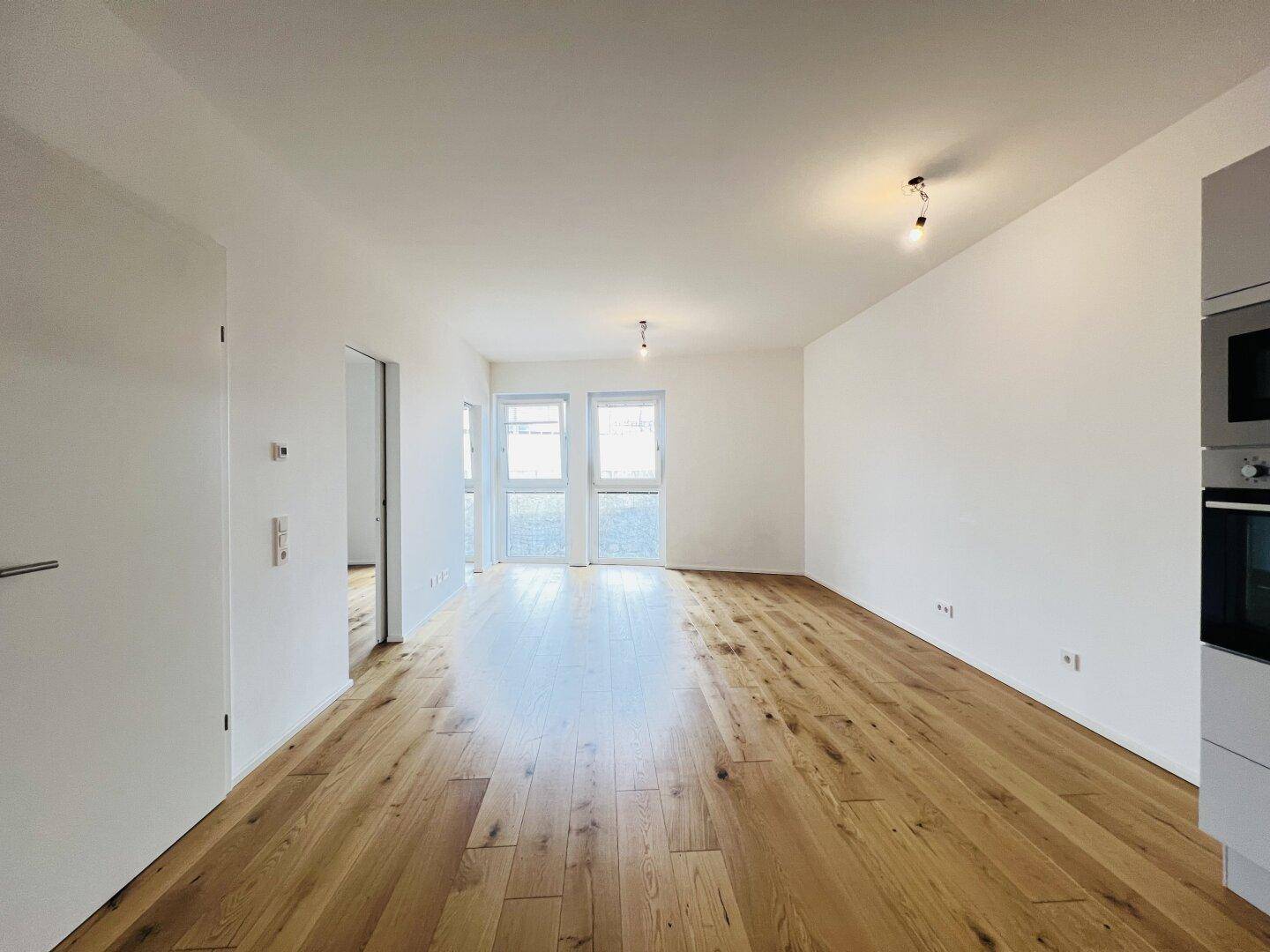 Heller Wohnbereich mit Holzboden und Zugang nach draußen, angrenzend an eine moderne Küchenzeile.
