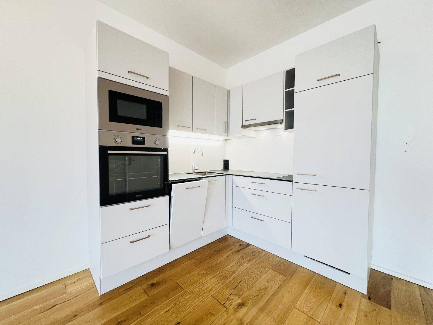 Moderne Einbauküche in Weiß mit integrierten Geräten und hellem Holzfußboden.