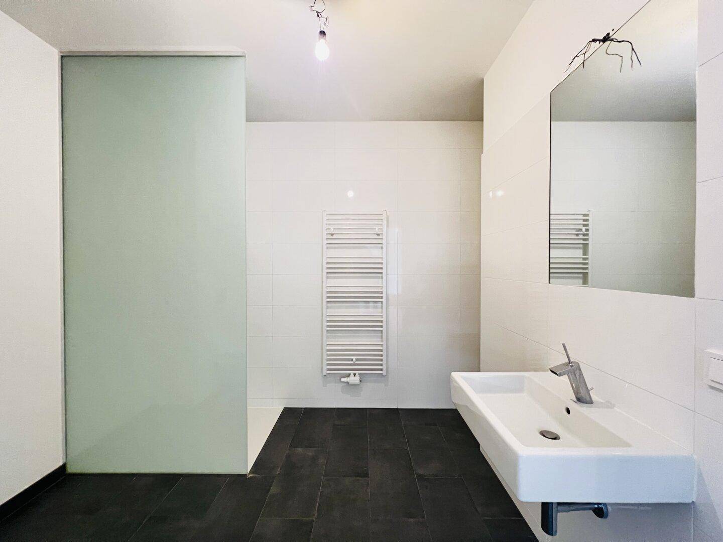Modernes Badezimmer mit weißen Fliesen, dunklem Boden, Einzelwaschbecken und Handtuchheizkörper.