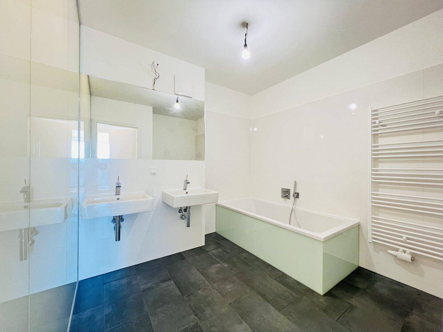 Modernes Badezimmer mit Doppelwaschbecken, Badewanne und dunklen Fliesen.