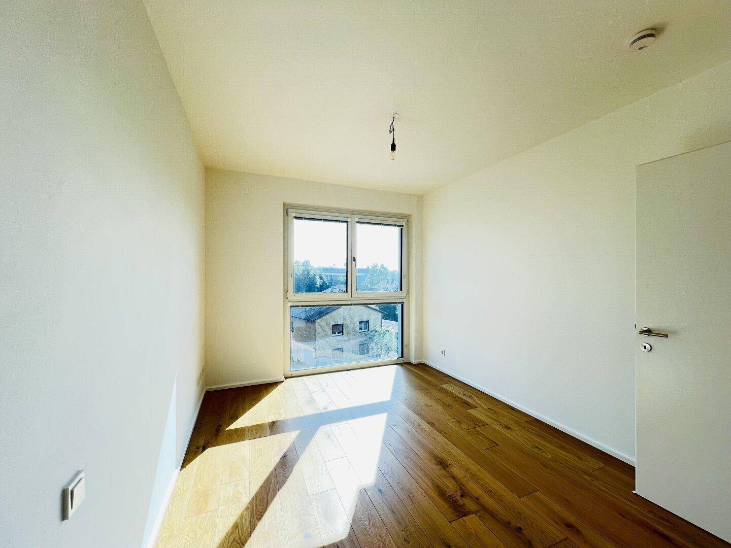 Sonniger Raum mit Holzboden und Fensterfront, die viel Licht spendet.