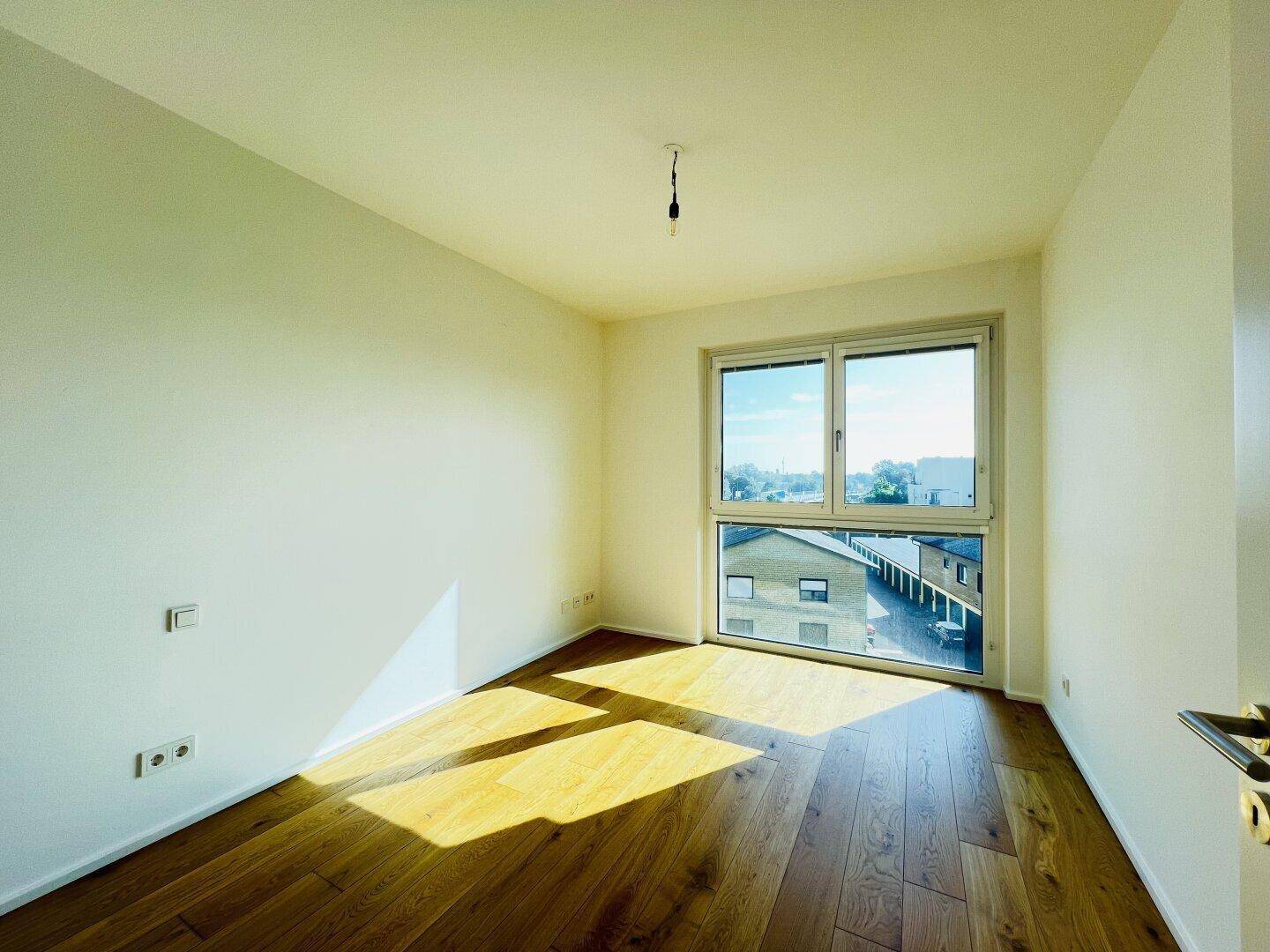 Geräumiges, helles Zimmer mit Holzboden und weitem Blick durch das große Fenster.