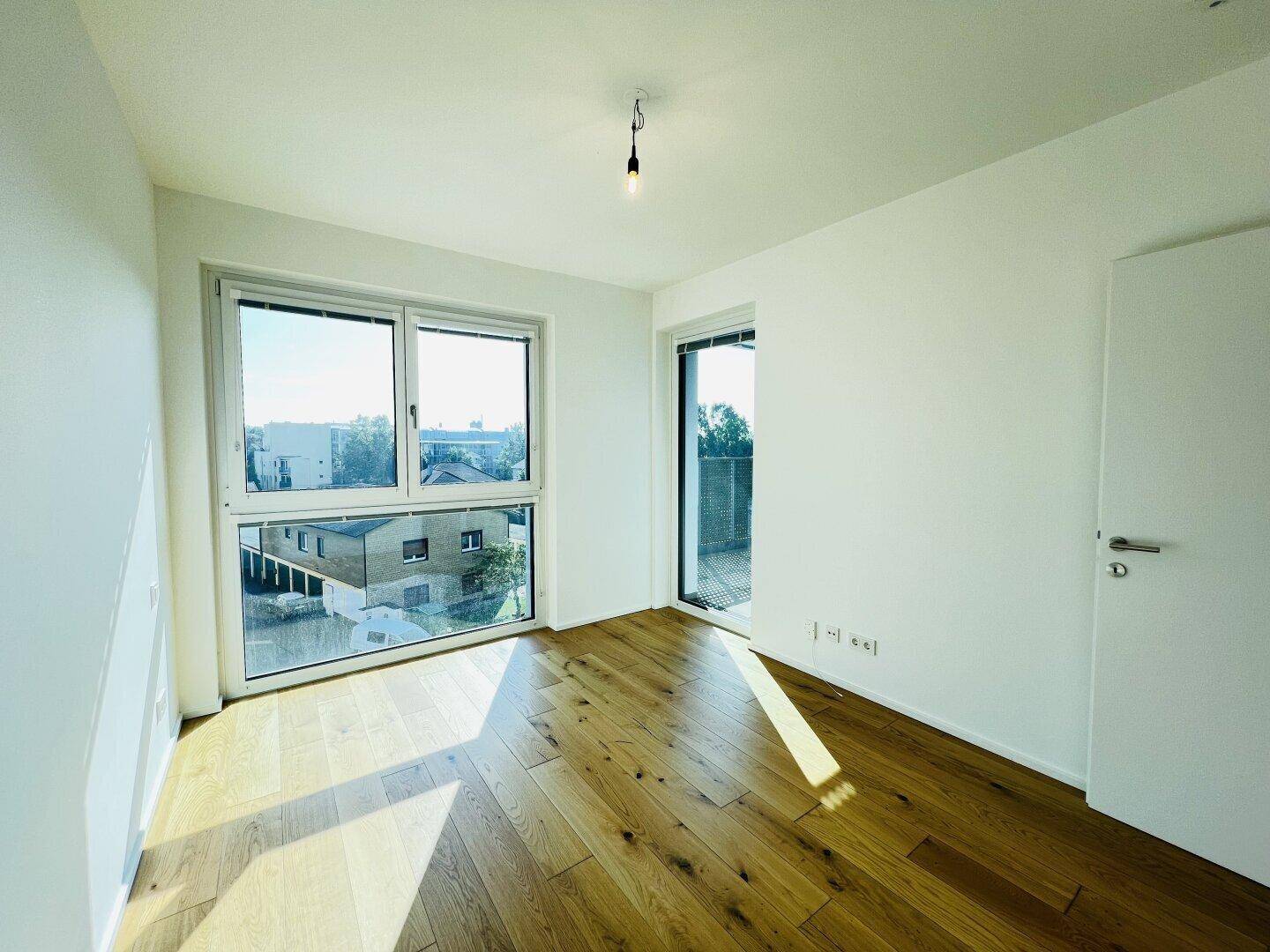 Lichtdurchflutetes Zimmer mit Holzboden und Zugang zu einem Außenbereich.