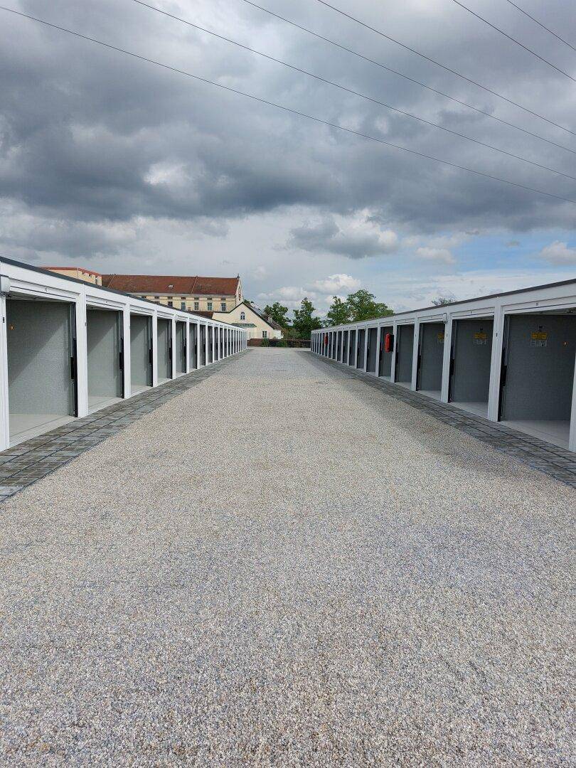 Lange Reihe von modernen Garagen oder Lagereinheiten mit offenen Toren unter einem bewölkten Himmel.