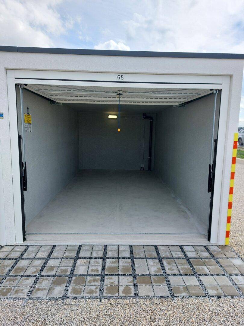 Innenansicht einer einzelnen, sauberen Garage mit Betonboden, Beleuchtung und einem geöffneten Rolltor.