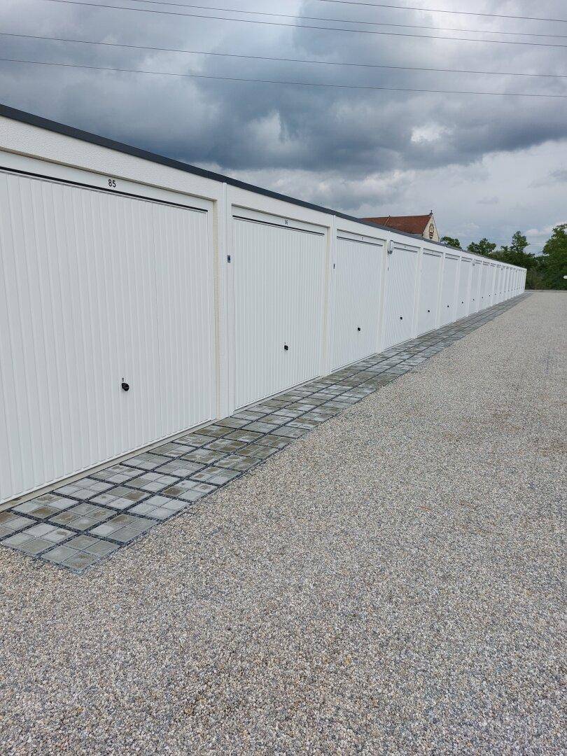 Seitenansicht einer langen Reihe von weißen Garagentoren und einem Schotterweg unter einem bewölkten Himmel.