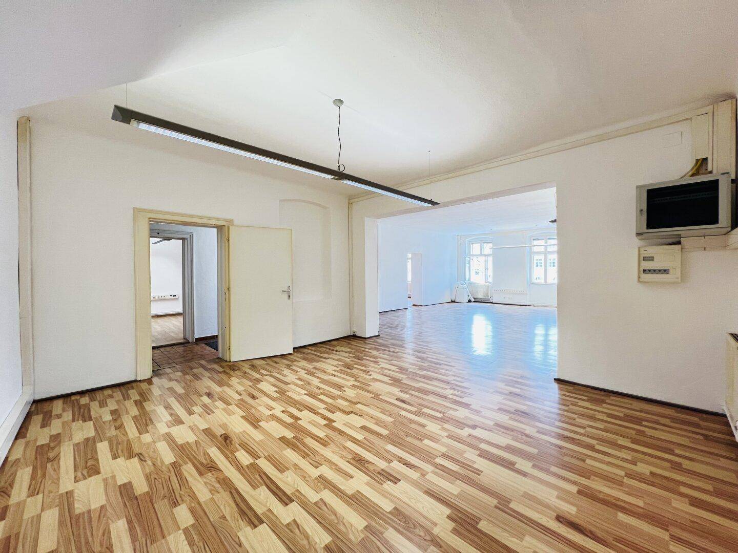 Heller Raum mit Laminatboden und offener Tür zu einem weiteren Zimmer, gut beleuchtet.