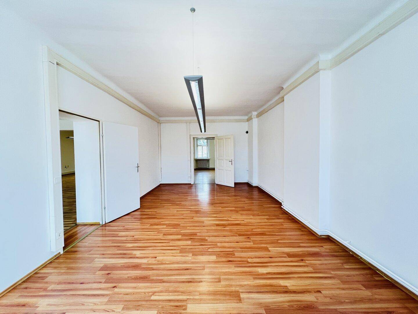 Langer, heller Raum mit Laminatboden und Türen an beiden Enden, ausgestattet mit Deckenleuchte.