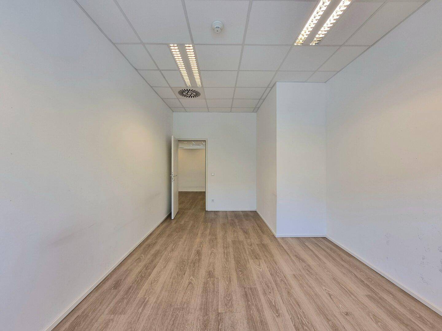 Helles, leeres Büro mit Holzfußboden, weißen Wänden und einer offenen Tür.