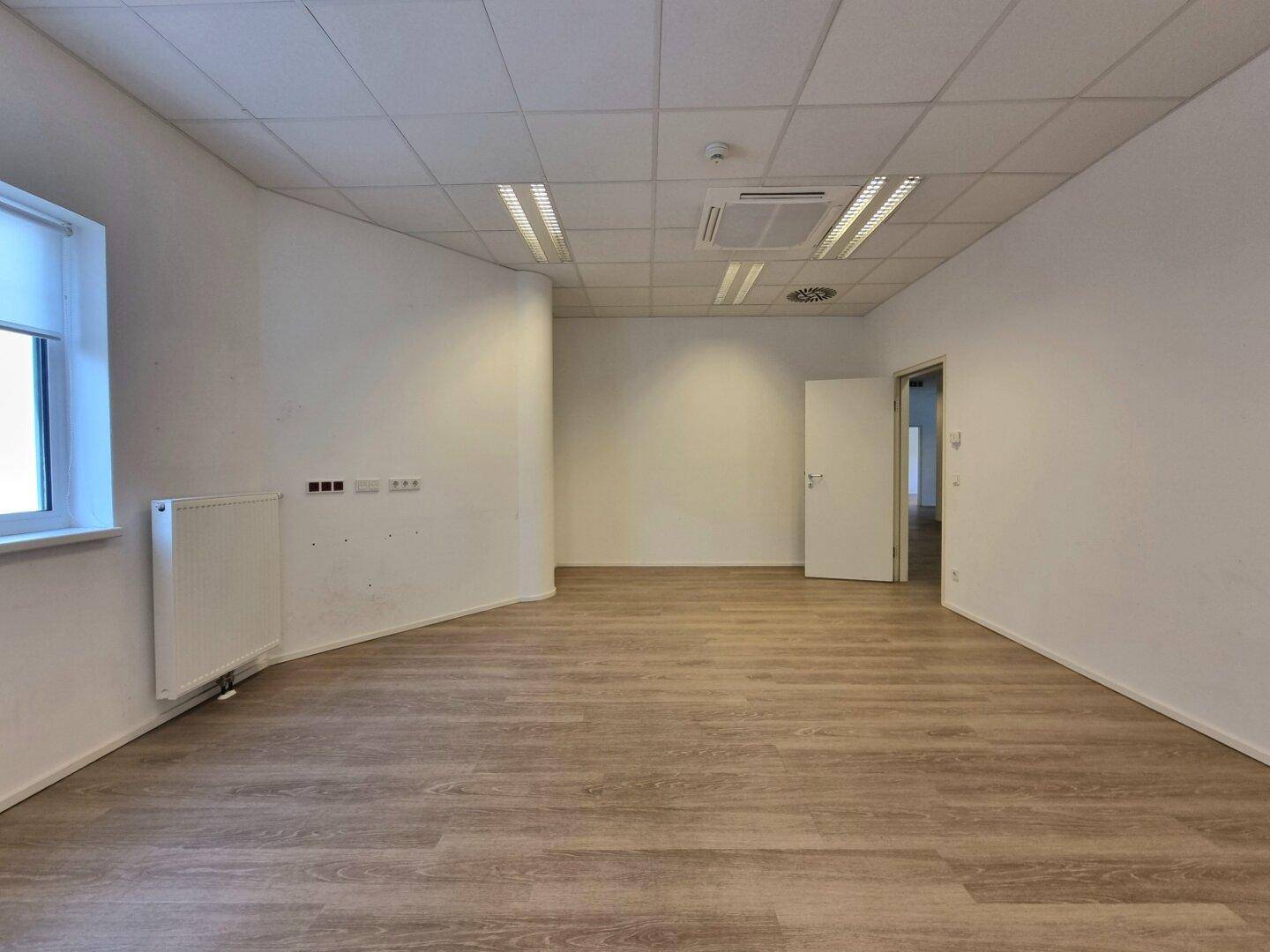 Helles Büro mit Fenster, Heizkörper und einem modernen Deckenklimasystem.