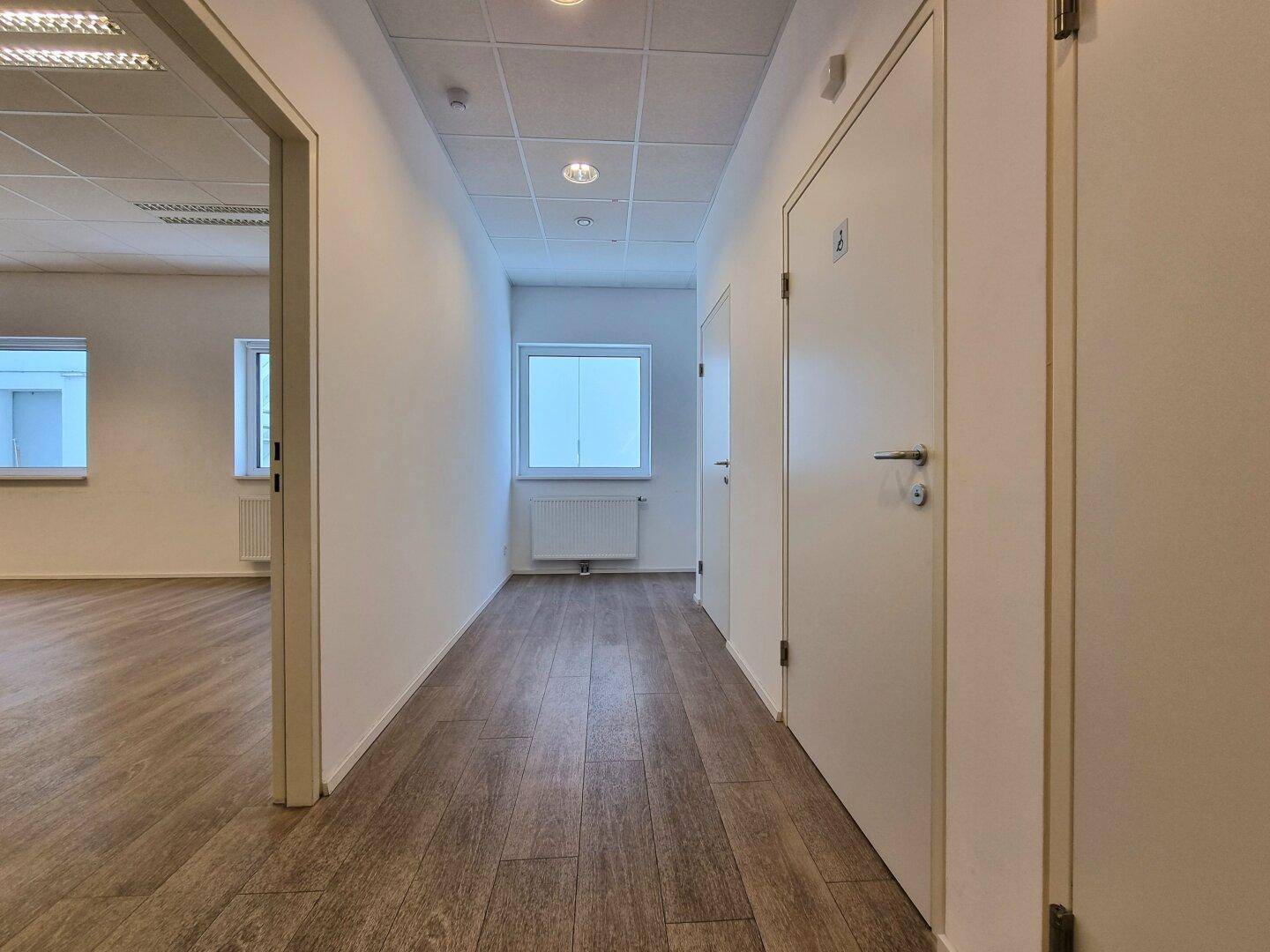 Heller Flur mit Laminatboden, weißen Wänden und mehreren Türen, der zu weiteren Räumen führt.