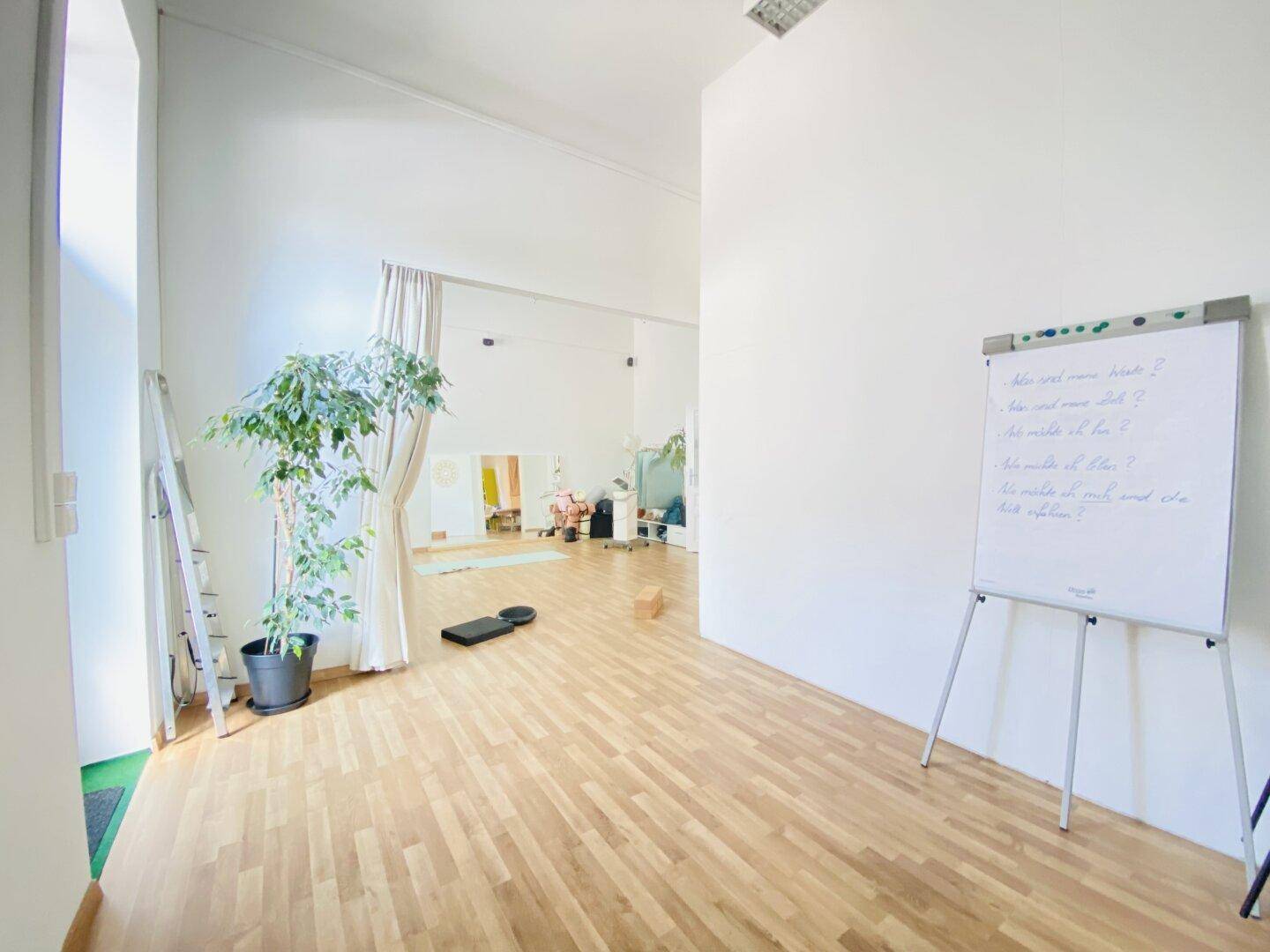 Geräumiger Studiobereich mit Holzboden, Whiteboard und Pflanzen, ideal für kreative oder sportliche Aktivitäten.