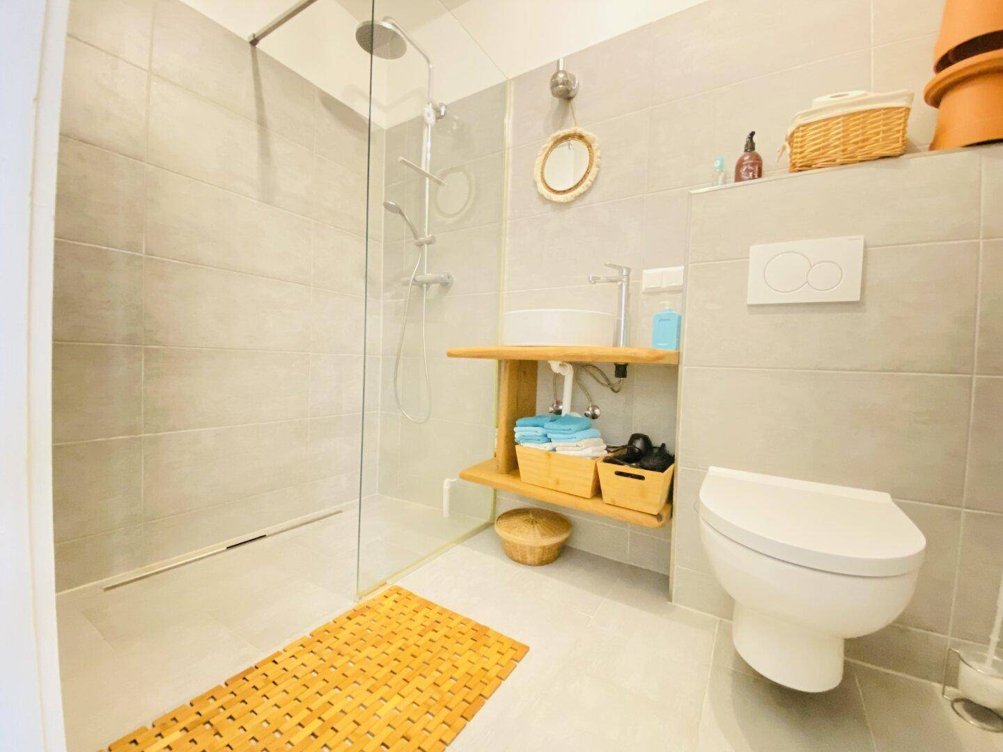 Modernes Badezimmer mit ebenerdiger Dusche, Hänge-WC und hellgrauen Fliesen, funktional und stilvoll.