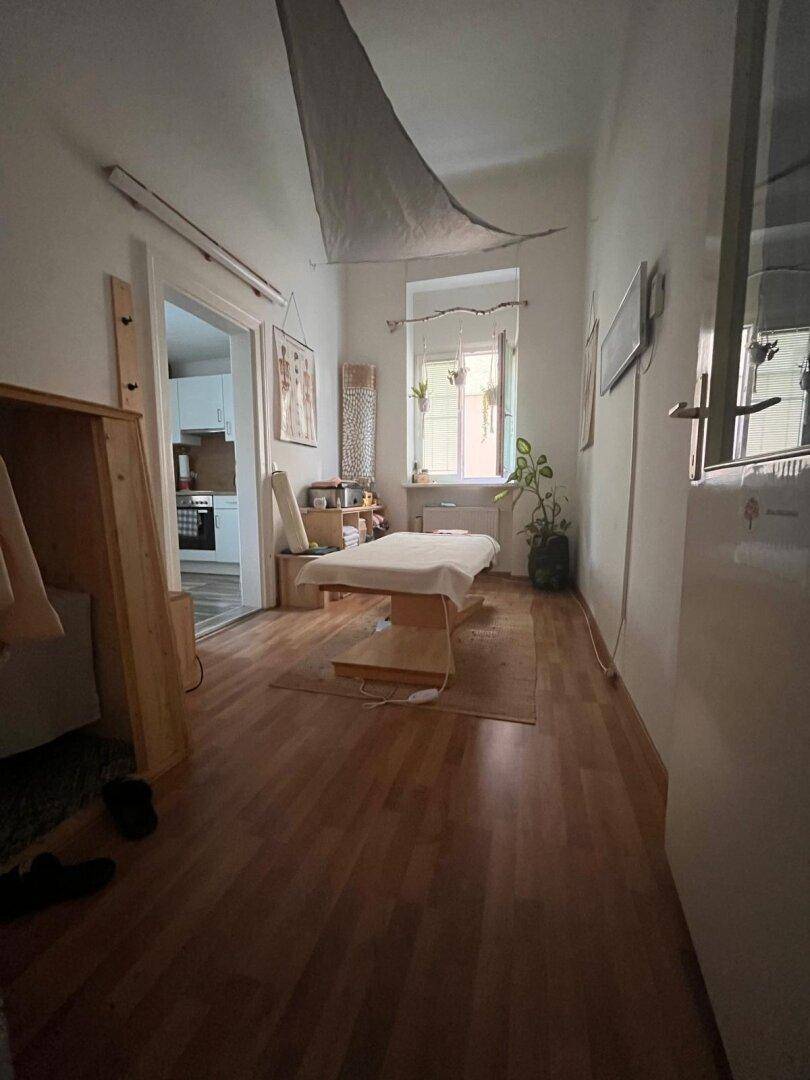 Gemütlicher Therapieraum mit Liege, Holzboden und Fenster, ideal für entspannende Behandlungen.