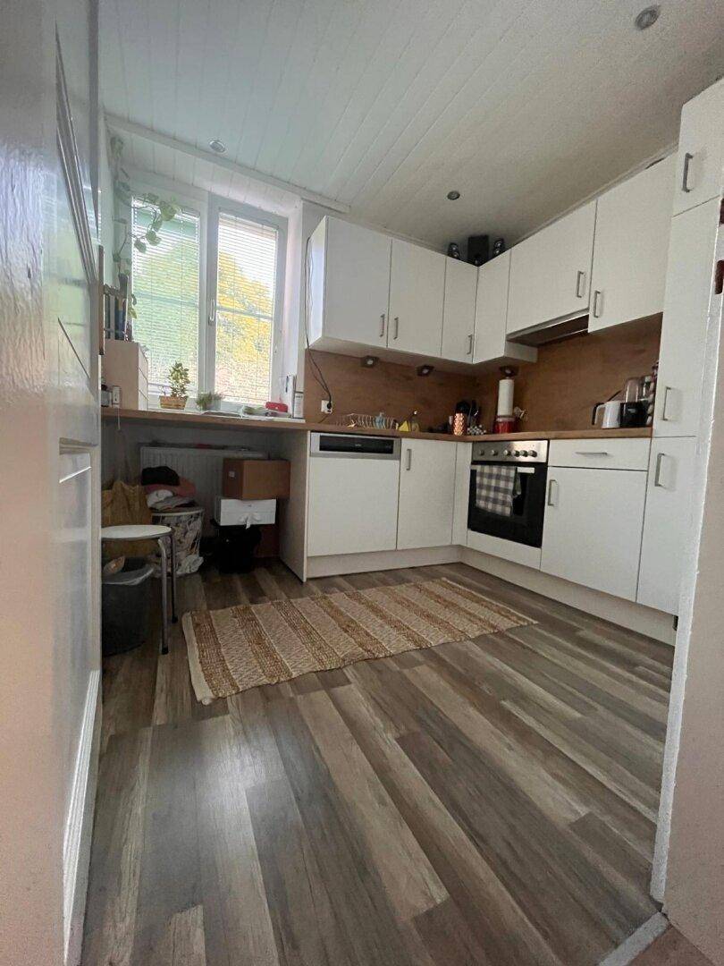 Funktionale Küche mit weißen Schränken, Holzrückwand, Fenster und Laminatboden, ausgestattet mit Geräten.