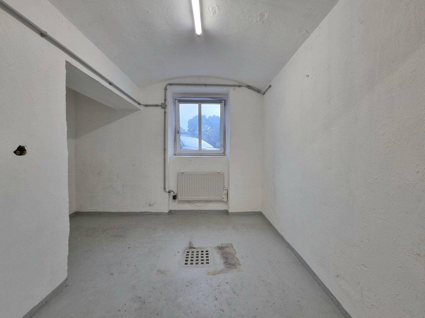 Funktionaler Kellerraum mit Betonboden, kleinem Fenster, Heizkörper und einem Bodenablauf für vielseitige Nutzung.