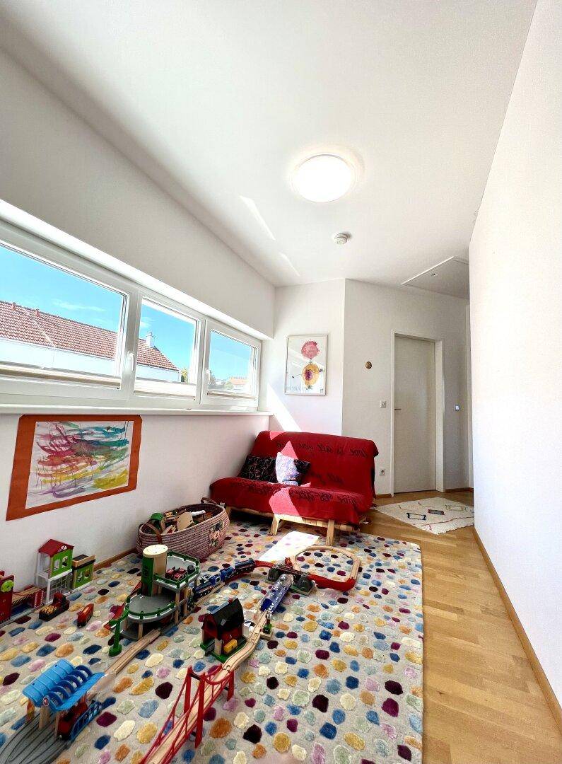 Helles Kinderzimmer mit Spielteppich, Sofa und großen Fenstern für viel Tageslicht.