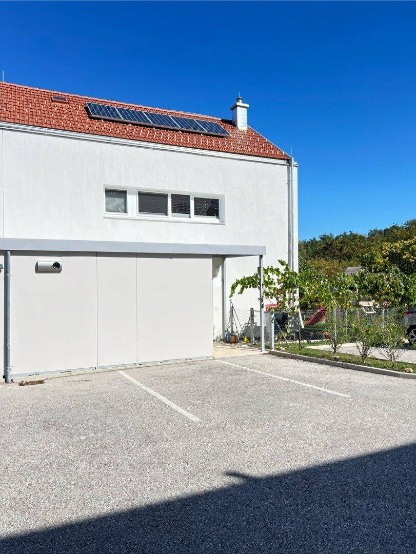 Weißes Wohnhaus mit rotem Ziegeldach, Solaranlage und Parkplätzen im Freien.