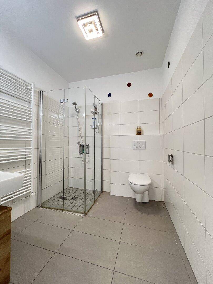 Modernes Badezimmer mit begehbarer Dusche, Wand-WC und beheiztem Handtuchhalter.