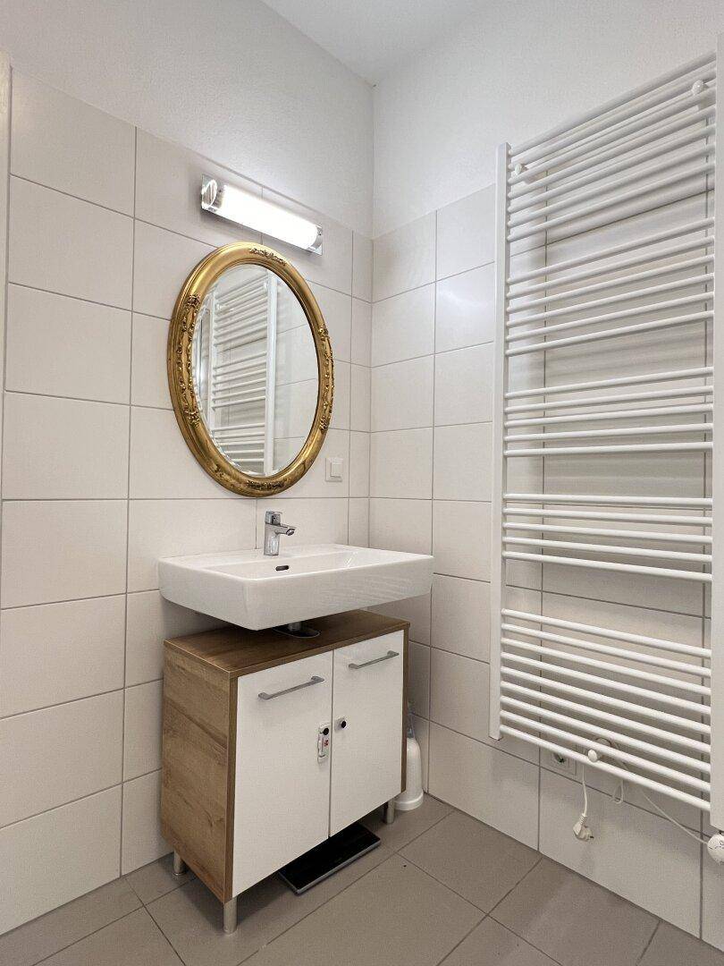 Helles Badezimmer mit modernem Waschtisch, ovalem Spiegel und beheiztem Handtuchhalter.