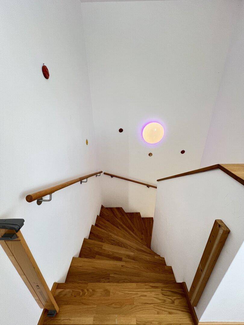 Holztreppe mit hellem Geländer, die in die oberen Stockwerke des Hauses führt.