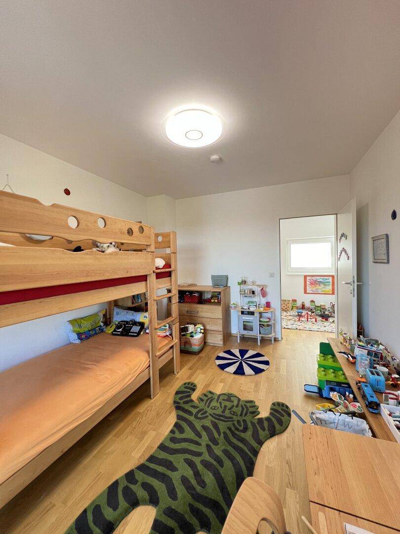 Geräumiges Kinderzimmer mit Etagenbett, Spielbereich und Zugang zu einem weiteren Raum.