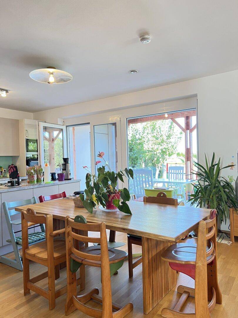 Heller Essbereich mit Holztisch und Blick auf die überdachte Terrasse und den Garten.