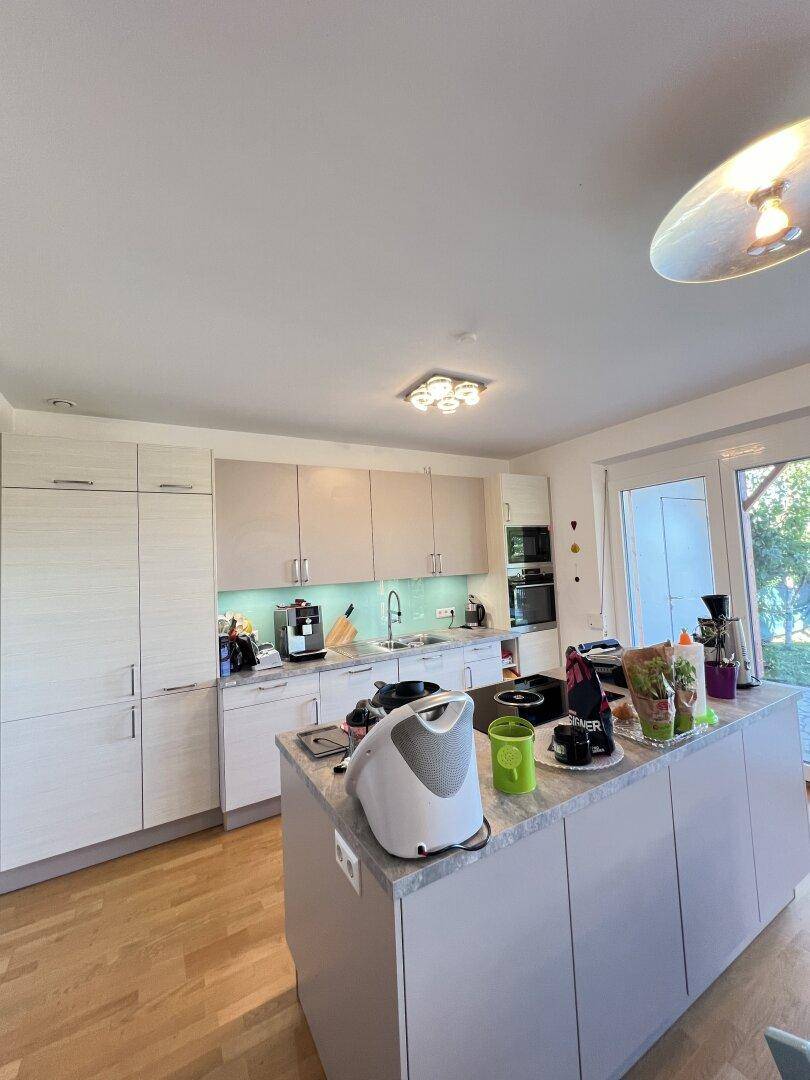 Moderne Küche mit heller Holzoptik, Kücheninsel und integrierten Geräten.