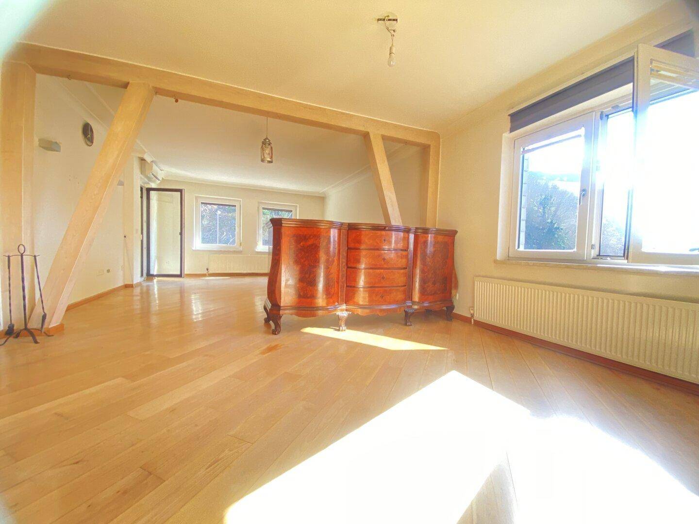 Helles Wohnzimmer mit Holzbalken, Parkettboden und antiker Kommode.