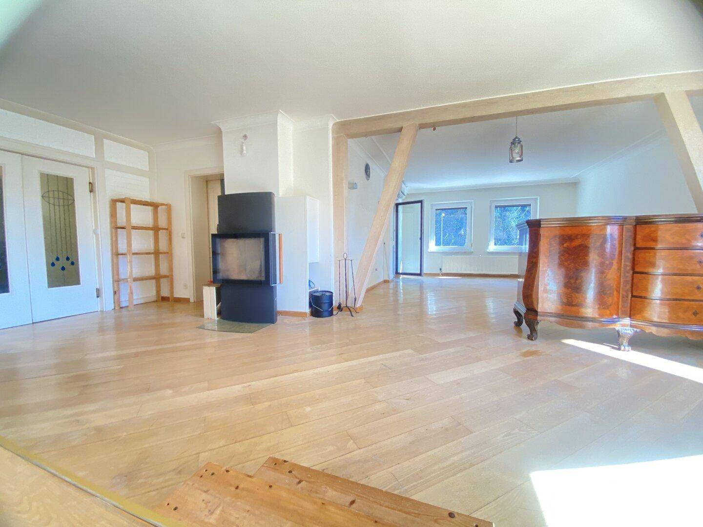Geräumiges Wohnzimmer mit Parkettboden, Kaminofen und Holzbalken.