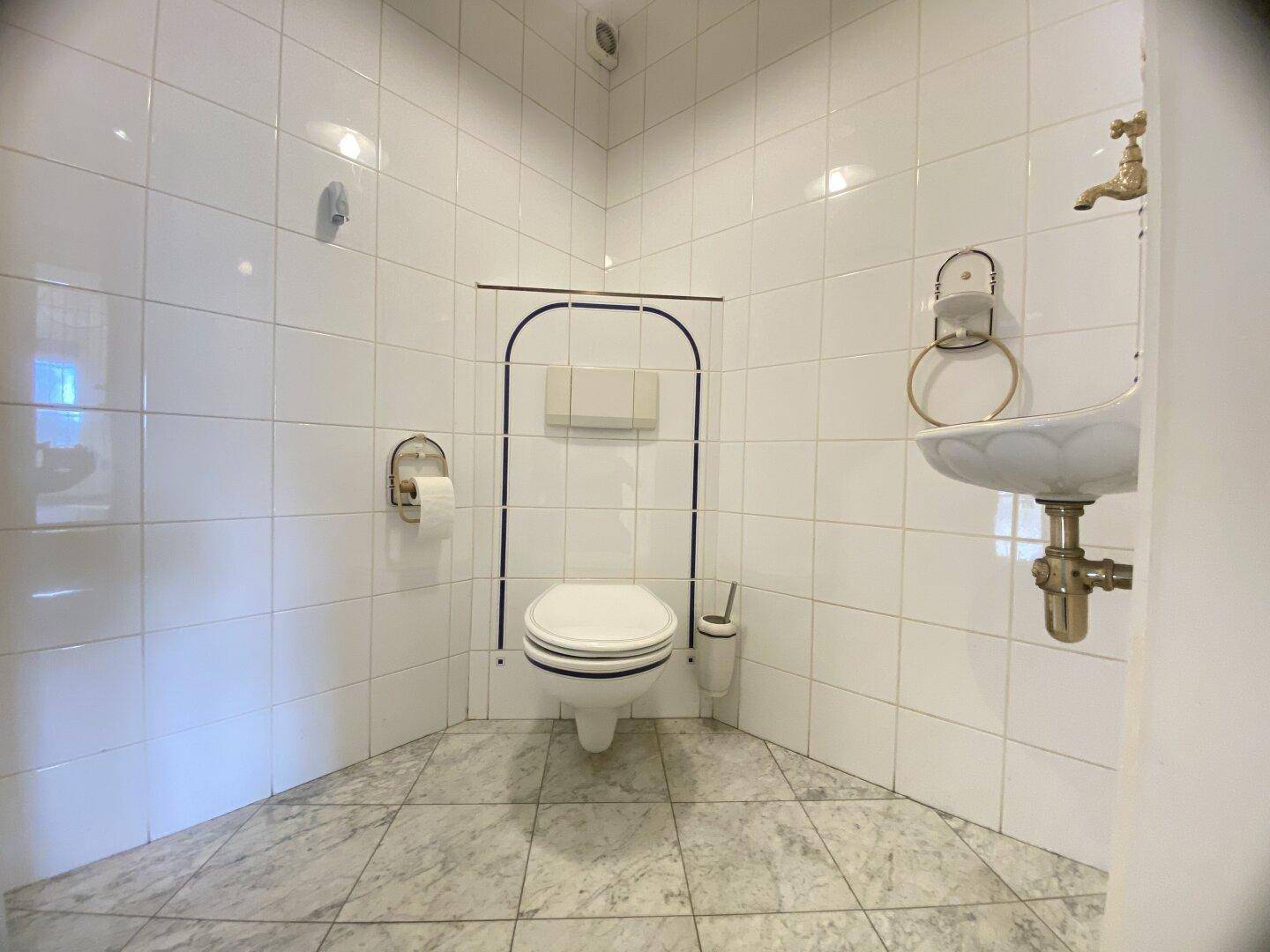 Gefliestes Gäste-WC mit Wand-WC und kleinem Waschbecken.