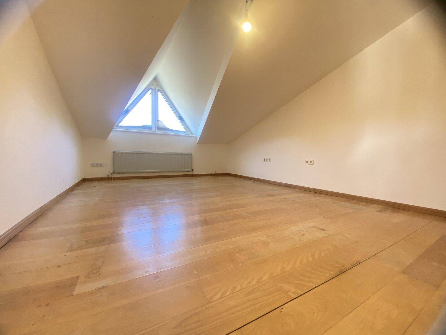 Helles Schlafzimmer im Dachgeschoss mit Parkettboden und dreieckigem Fenster.