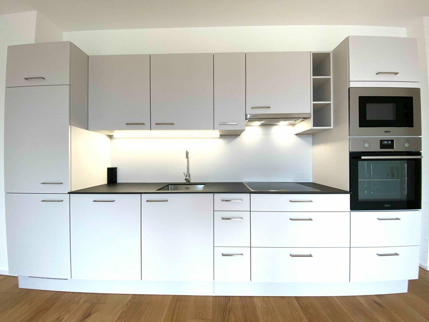 Moderne Einbauküche mit weißen Schränken, dunkler Arbeitsplatte und integrierten Geräten.